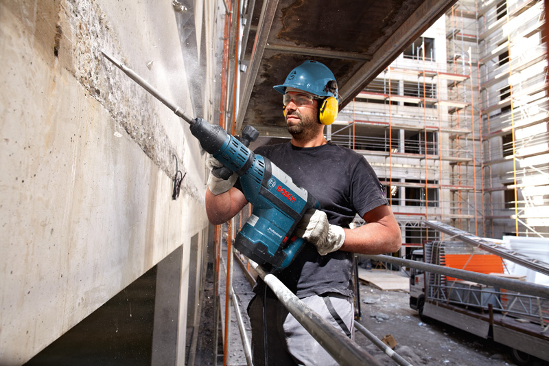 Eine Person mit Sicherheitsausrüstung verwendet einen Abbruchhammer, um auf einer Baustelle Beton aufzubrechen. Anwendungsbild
