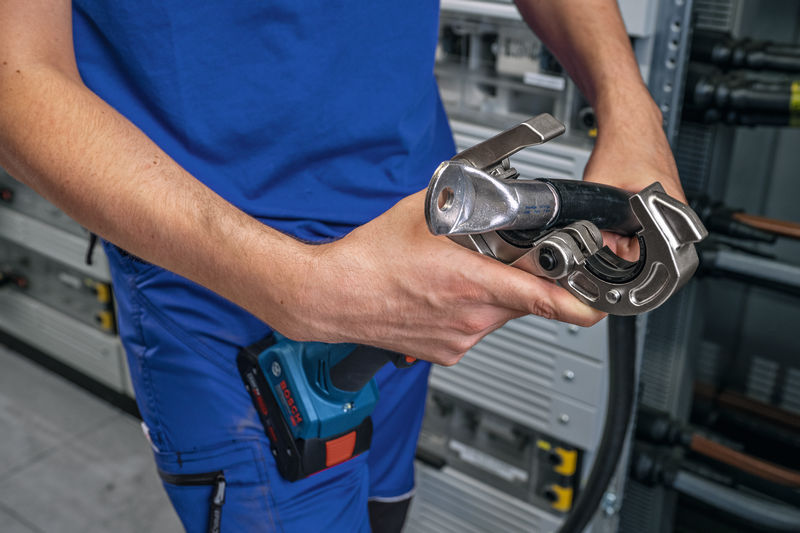 Eine Person mit Sicherheitsausrüstung verwendet ein kabelloses hydraulisches Crimpwerkzeug an einem Kabel. Anwendungsbild